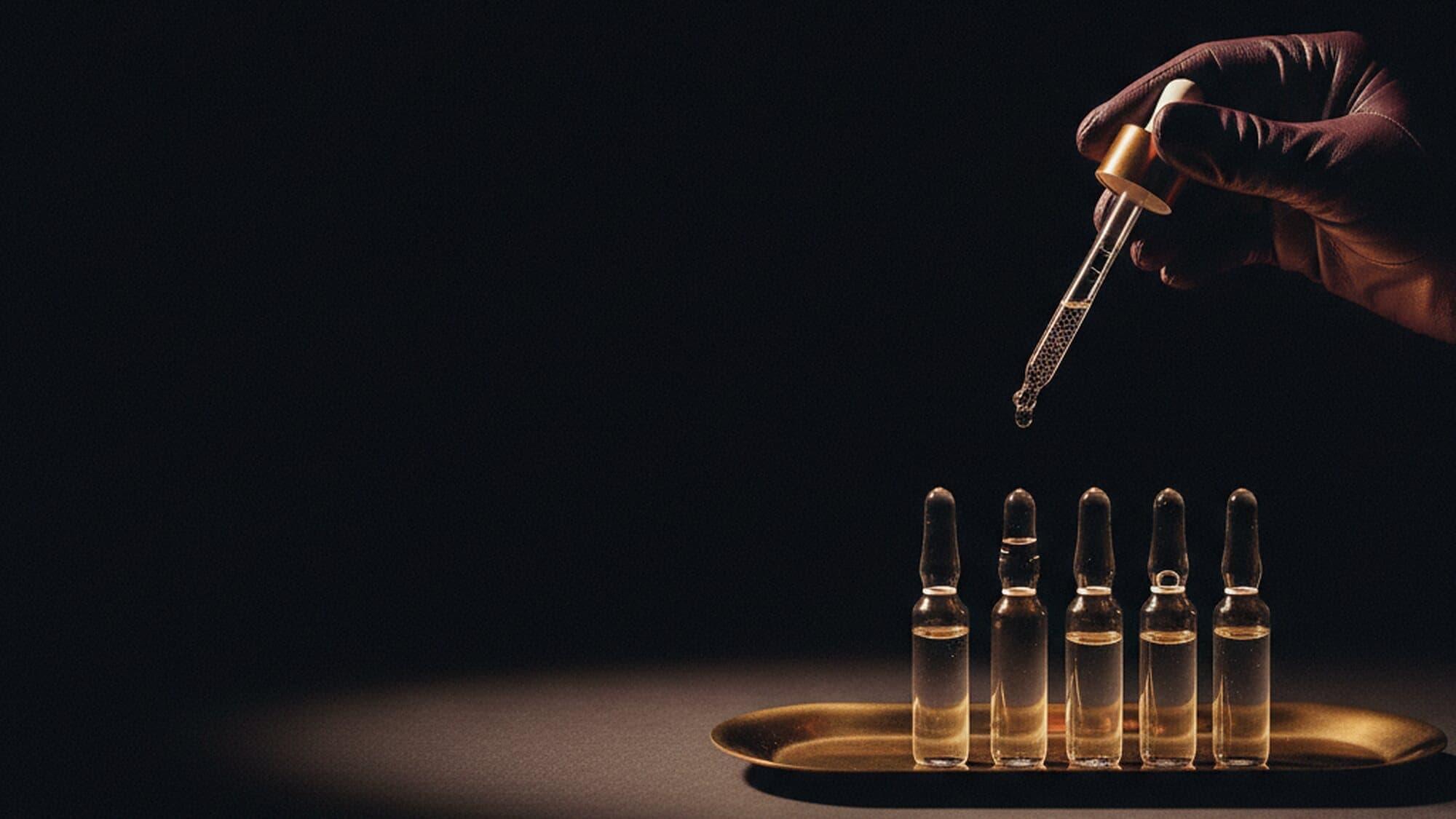 Eine Reihe Wirkstoff-Ampullen auf einer flachen Messingschale, eine Hand setzt eine Pipette an